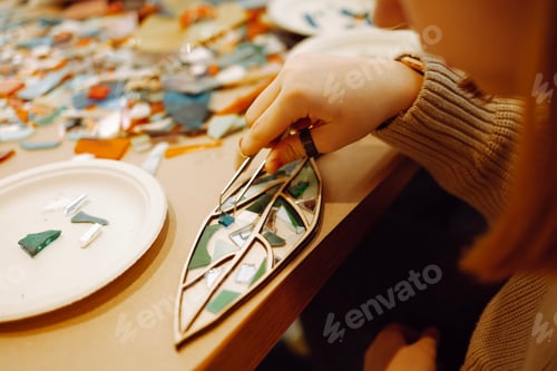 Preview: Closeup of female hand with rings holding glass piece with tweezers while making mosaic.