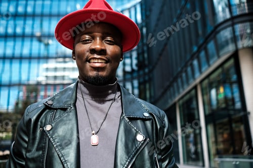 Vista previa: Un hombre sonriente con un sombrero rojo mira a la cámara de pie en un entorno empresarial exterior.