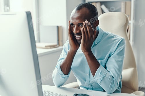 Preview: Handsome young African man in shirt keeping head in hands and smiling while working in the office