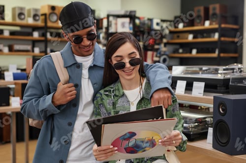 Preview: Multiethnic young couple holding vinyl records in music store and smiling