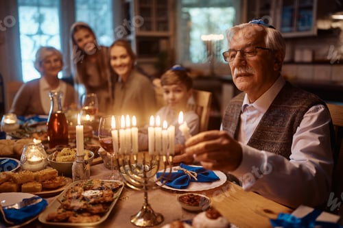 Preview: Close up of senior Jewish man lighting the menorah during family dinner on Hanukkah.