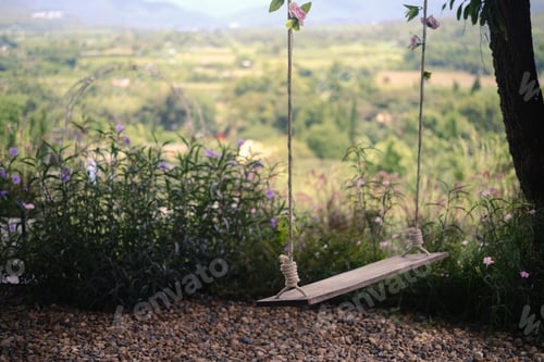 Preview: Wooden swing hanging from tree branch with beautiful views on background.