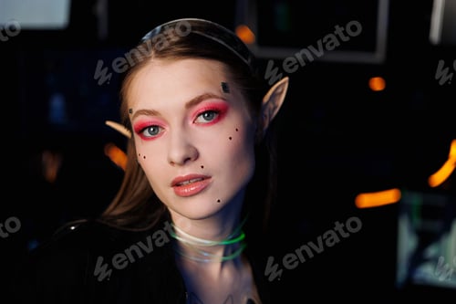 Preview: Cosplay girl with artistic make-up in glasses with elf ears in coloured light