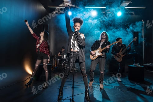 Preview: Female singer with microphone and rock and roll band performing hard rock music on stage