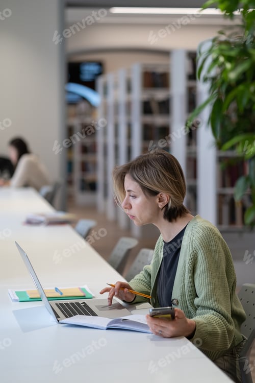 Preview: Focused female university teacher using laptop while sitting in quiet cozy library