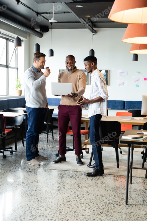 Preview: Surprised african american businessman with laptop by colleagues in office