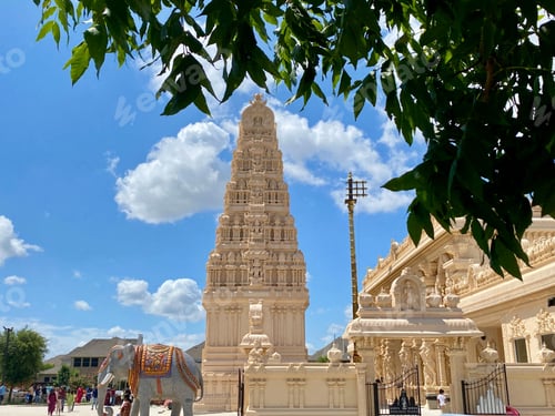 Preview: Vibrant Hindu temple with intricate architecture, clear blue sky, and lush green foliage