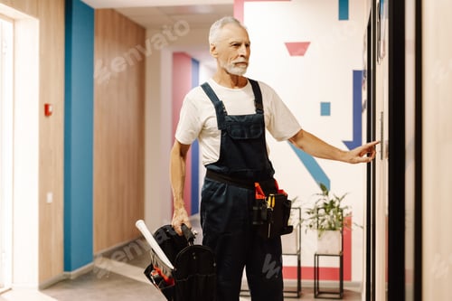 Preview: Senior, gray haired hHandyman with tool bag ringing doorbell at customer's home