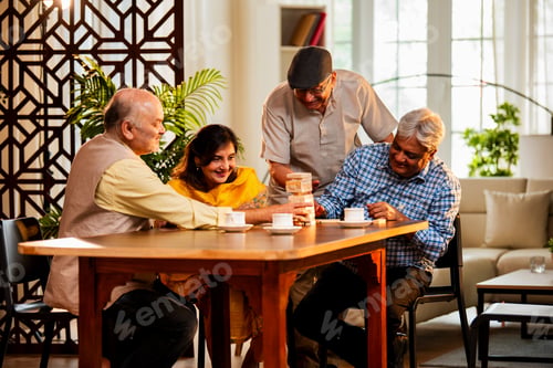 Preview: Indian senior adults playing jenga game and bonding while seated together at indoor dining table