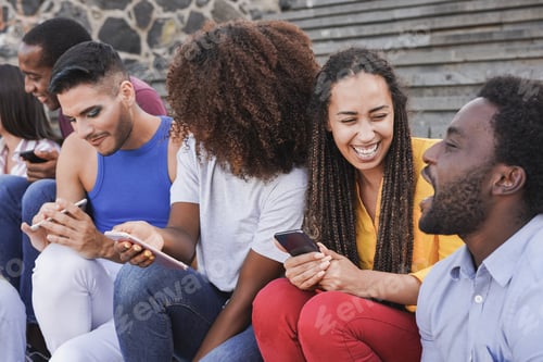 Preview: Young multiracial people having fun in the city sitting on stairs and using mobile phone