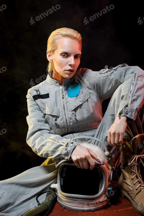 Preview: attractive female astronaut in spacesuit holding helmet and sitting on planet