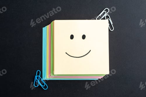 Preview: Top view of smiling emoji face on small note sheet paper clips on black background with free space