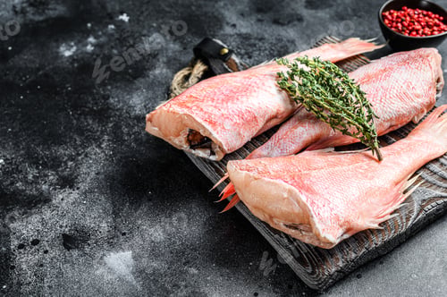 Preview: Whole raw red snapper fish on a cutting board. Black background. Top view. Copy space