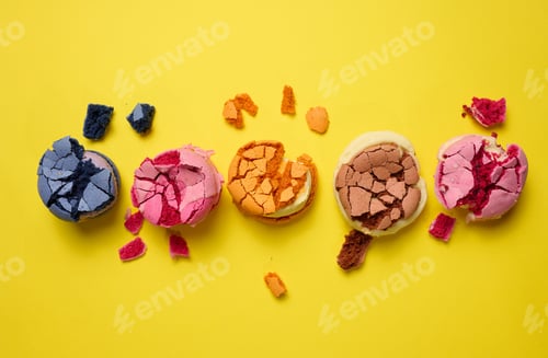 Preview: broken round macarons with crumbs on a yellow background, delicious dessert, top view
