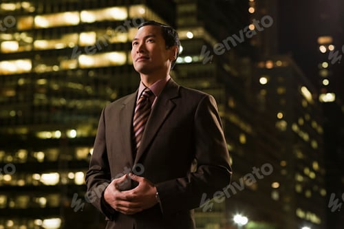 Preview: Confident businessman standing against a backdrop of city lights at night.