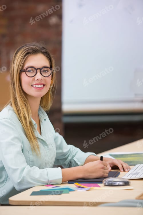 Preview: Woman in twenties smiling at camera, holding stylus, working on graphics tablet at desk, copy space