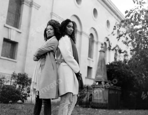 Preview: Confident couple of female friends posing back to back in front of old building.
