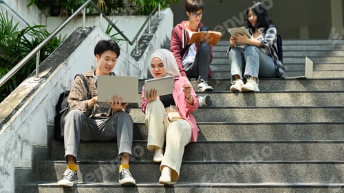 Preview: Group of university students sitting on stairs and talking to each other after classes.