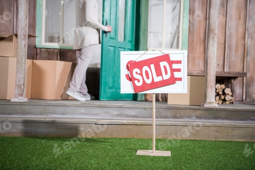 Preview: Cropped shot of senior woman standing in doorway of new house near sold sign on grass