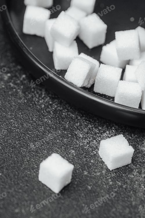 Preview: Cubes of sugar scattered on a dark surface in a minimalistic setting