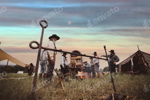 Preview: Oldest smart cowboy wearing western style with cowboy hat hold a cup drinking coffee on fire camp ea