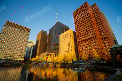 Preview: Buildings surrounded by vibrant golden autumn trees, under a clear blue sky with warm sunlight high