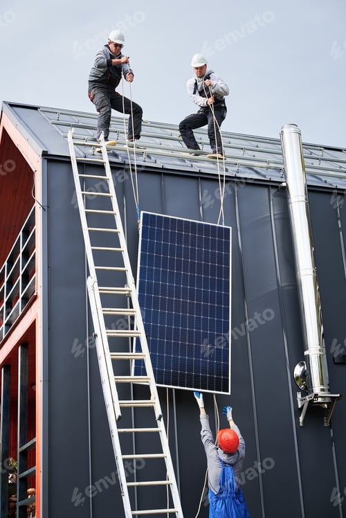 Preview: Workers lifting up photovoltaic solar module while installing solar panel system on roof of house.