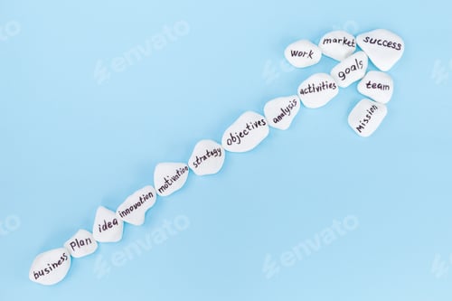 Preview: Top view of white stones with business lettering laid out in the form of an arrow