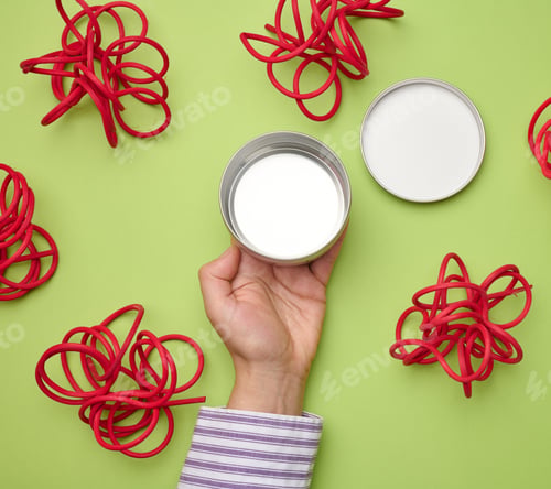 Preview: Female hand holds empty white iron jar for cosmetics. Packaging for cream, gel