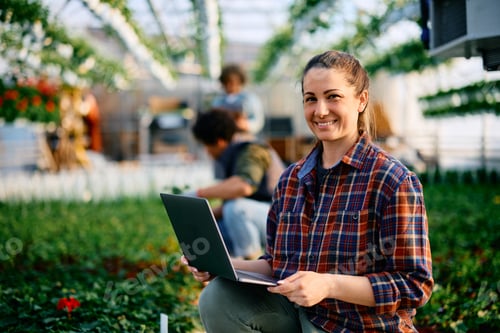 Preview: Happy plant nursery worker using laptop and looking at camera.