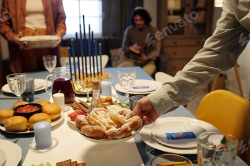 Preview: Hand of young man putting plate with homemade donuts on served table