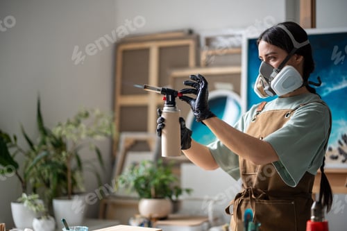Preview: Serious cautious artistic woman sets up gas burner before starting work on epoxy resin artwork.