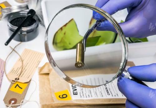 Preview: Expert police examines a bullet cap in scientific laboratory with magnifying glass