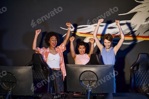 Preview: multicultural happy women looking at computer monitor and celebrating victory, raised hands