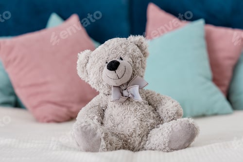 Preview: Close up horizontal view of teddy bear sitting on the bed with pillows on background