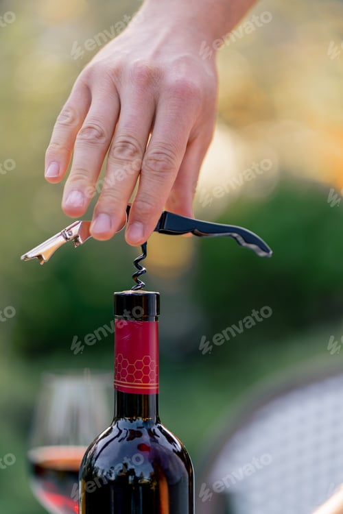 Preview: Close-up shot of a male sommelier's hand using a corkscrew to unscrew the wooden cork of wine bottle