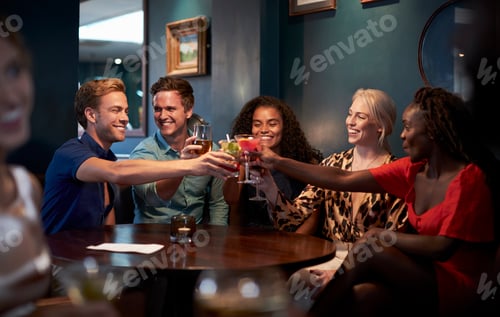 Preview: Group Of Young Friends Sitting Around Table And Making A Toast In Bar On Night Out