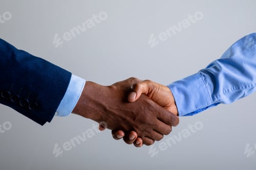 Preview: Mid section of two businessman shaking hands against grey background