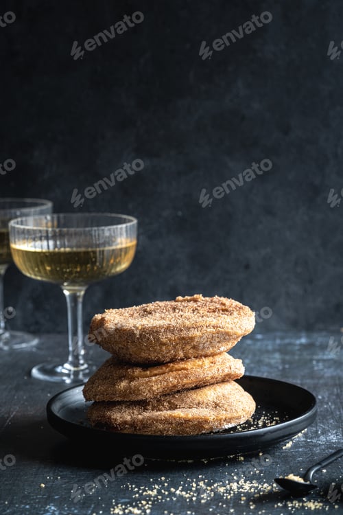 Preview: A stack of three apple beignets (apple fritters) on black background with glass of champagne