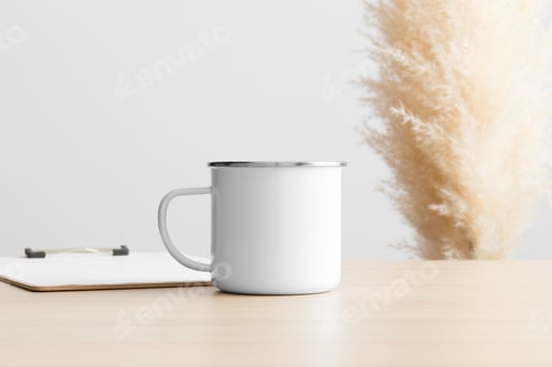 Preview: Enamel mug mockup with a clipboard on the wooden table with a pampas decoration.