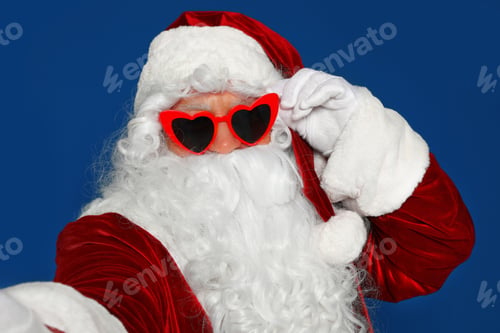 Preview: Authentic Santa Claus in sunglasses taking selfie on blue background