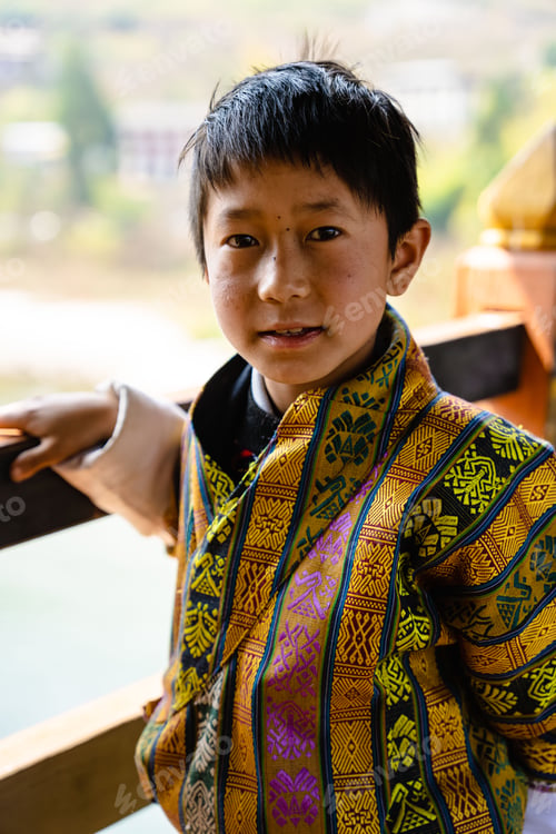 Preview: Young boy in traditional attire by a wooden railing.