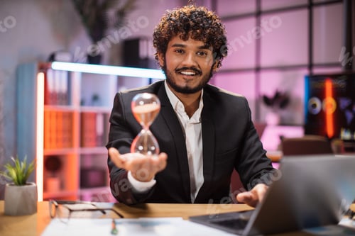 Preview: Confident businessman in formal suit sitting at desk with modern laptop and holding hourglass