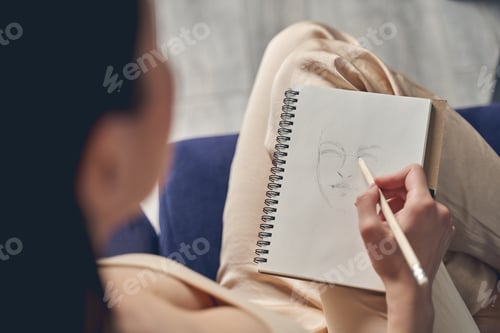 Preview: Young woman drawing in notebook at home