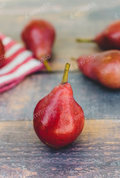 Preview: Juicy ripe red pears, fresh fruit on a rustic wooden table with striped towel in the background