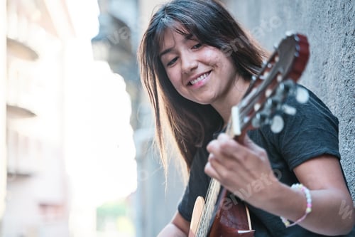 Preview: portrait of a brunette-haired latina woman playing the guitar. side view of a pretty woman smiling.