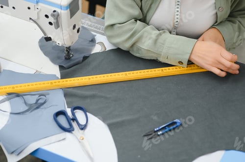 Preview: Young dressmaker woman sews clothes on working table.