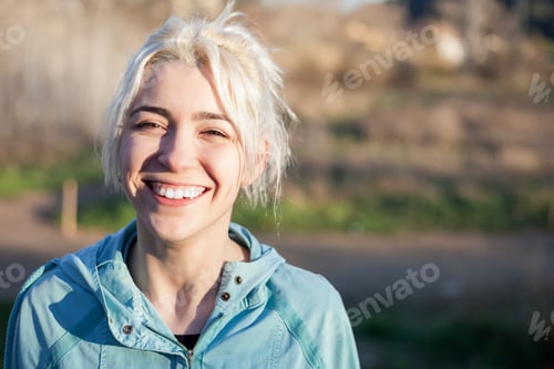 Preview: Smiling blonde looking at camera in a park on a sunny day