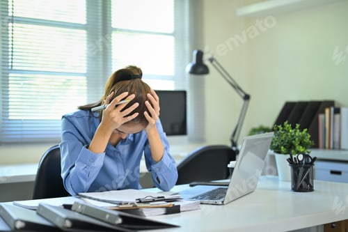 Preview: Frustrated businesswoman holding head in hands while working at desk