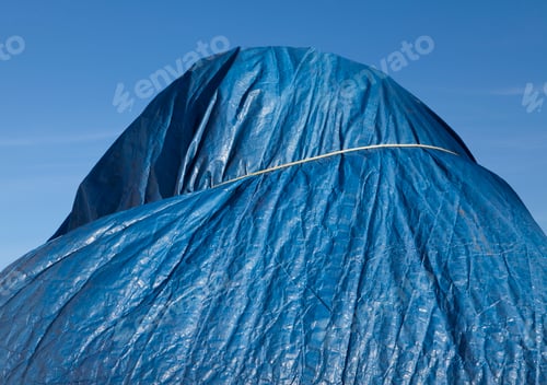 Preview: Low angle view of a blue tarpaulin, tied around a heap.